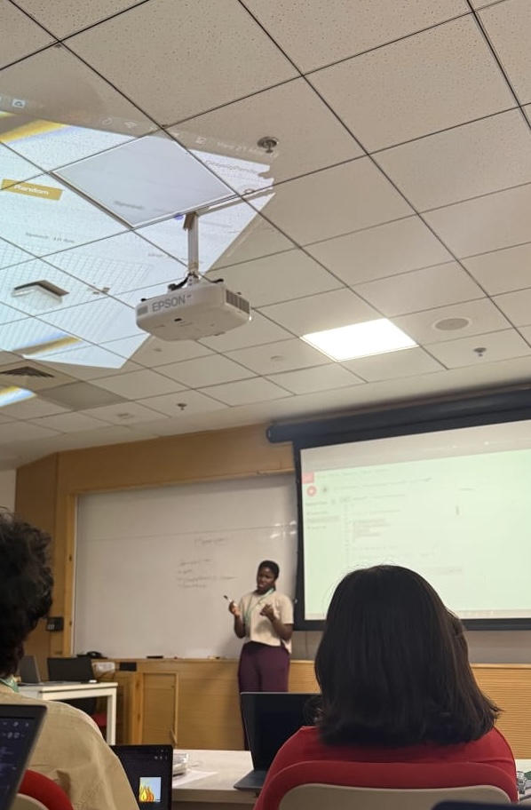 Yesirat Sanni teaching from the front of the classroom, students visible working on laptops in the foreground